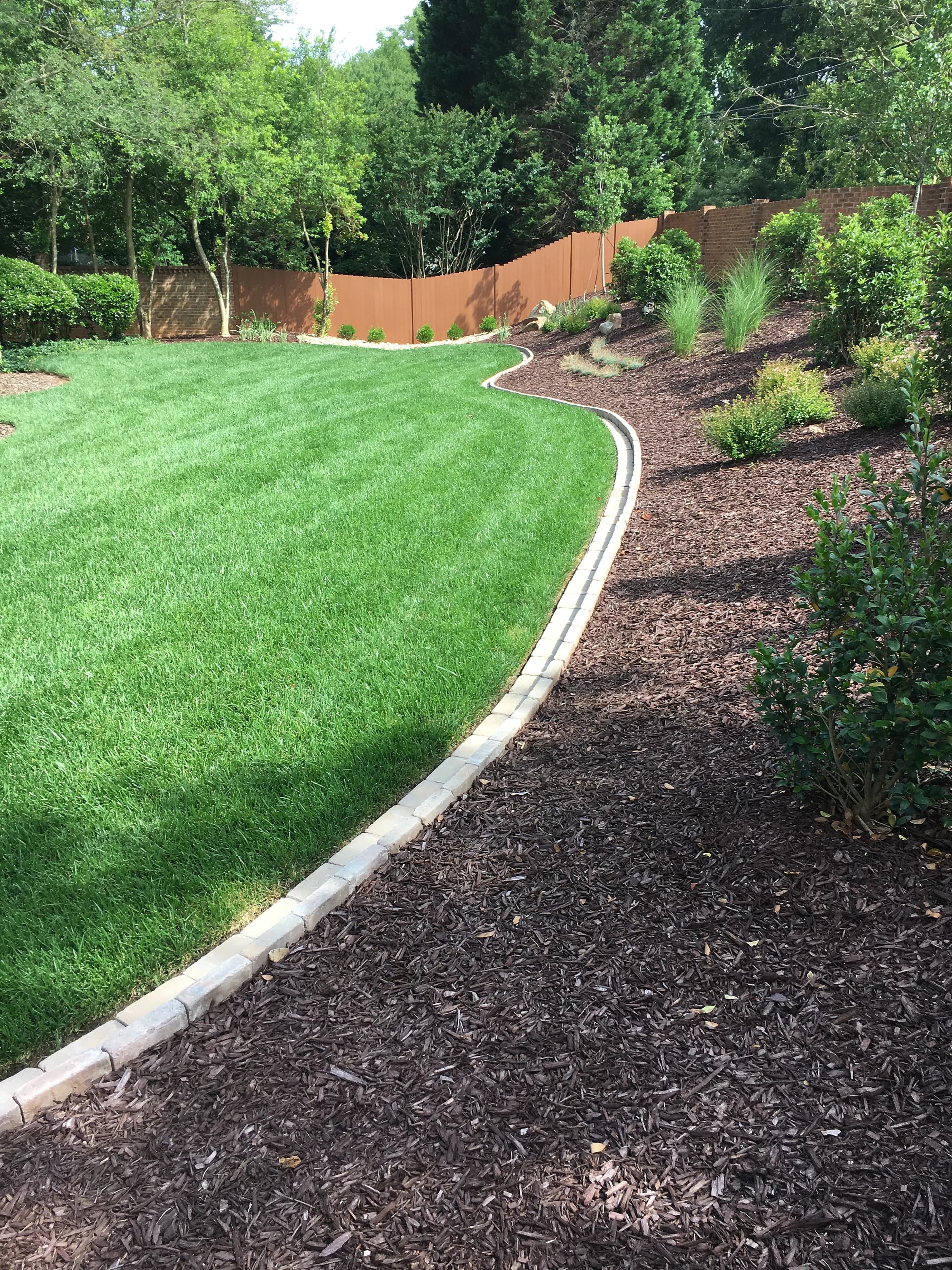A wide lawn edged in cut stone against a freshly mulched planting bed