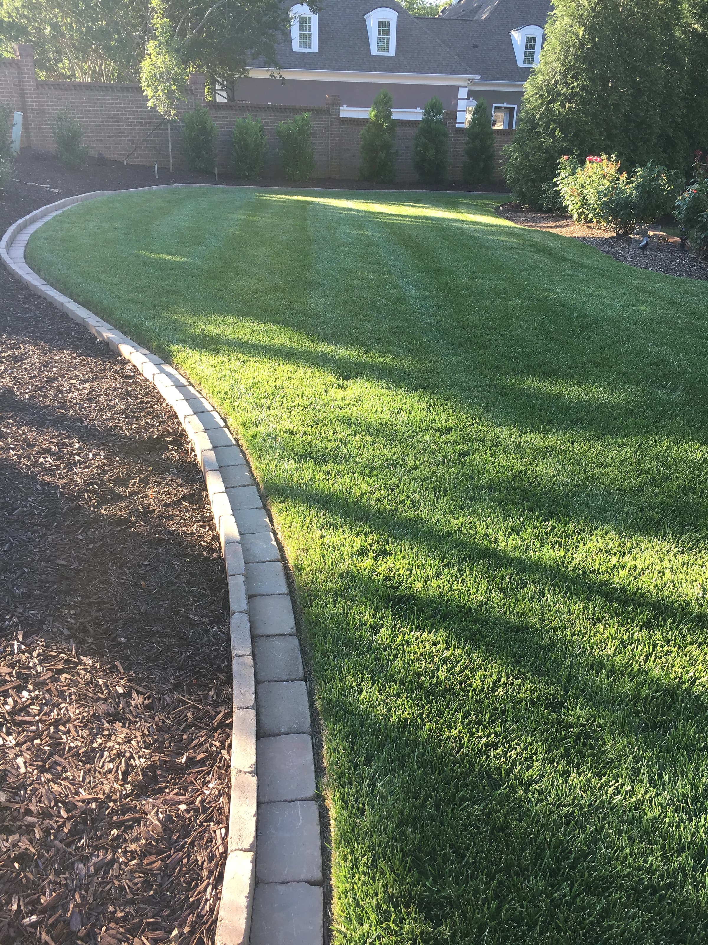 A stone-edged lawn curving away beside a deep, freshly mulched bed