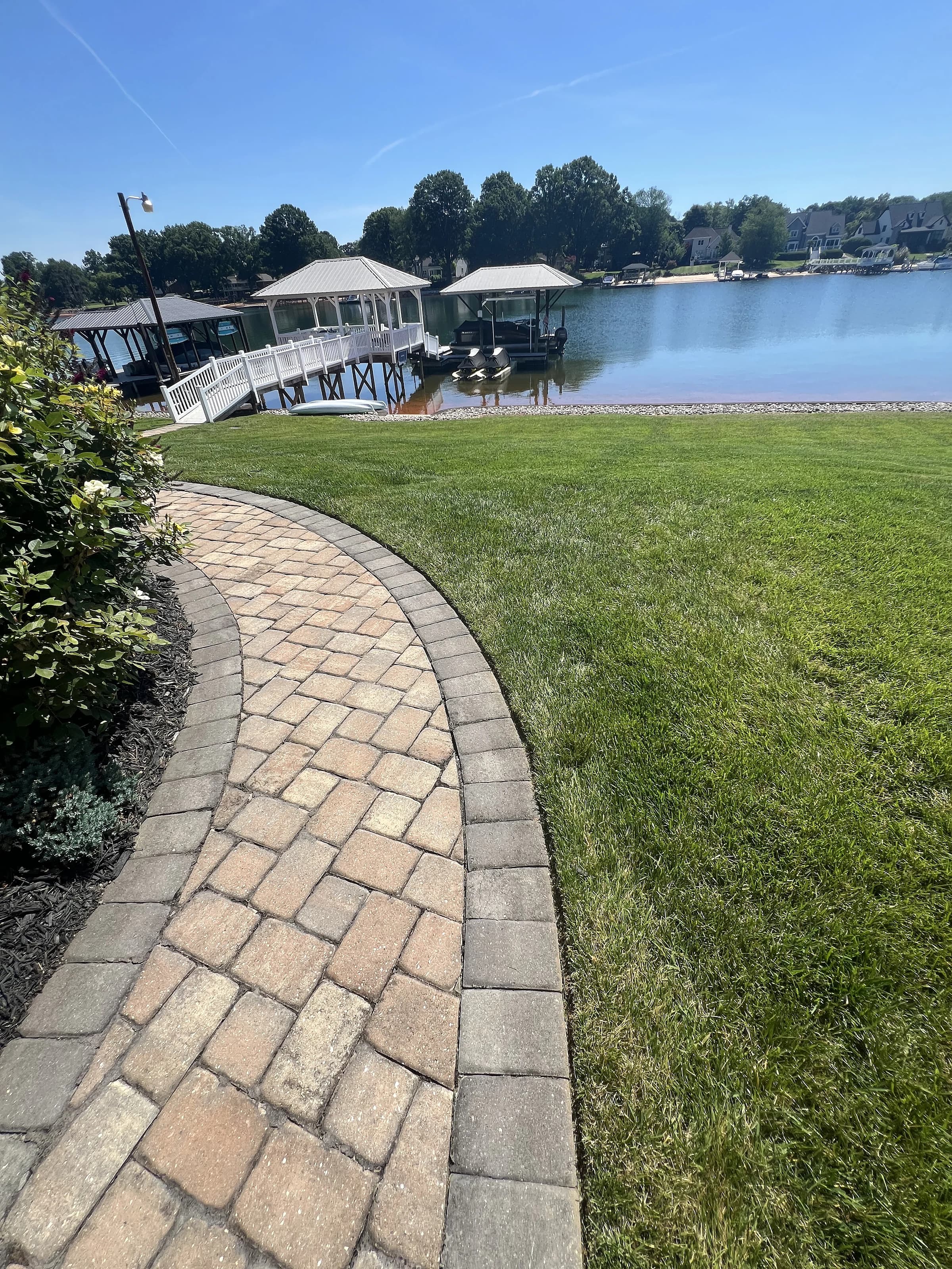 A paver walkway curving across a manicured lawn down toward the lake