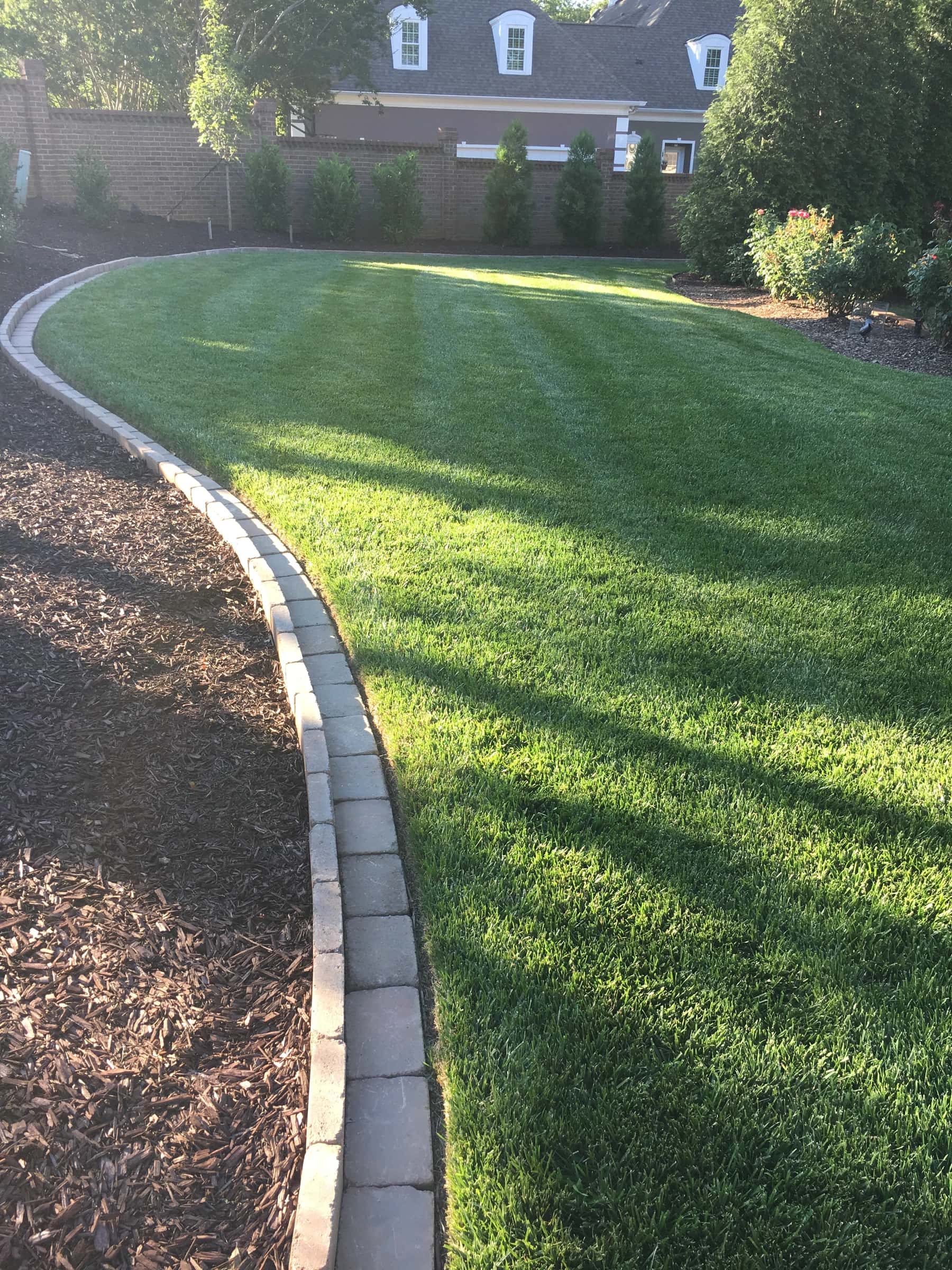 A stone-edged lawn curving away beside a deep, freshly mulched bed