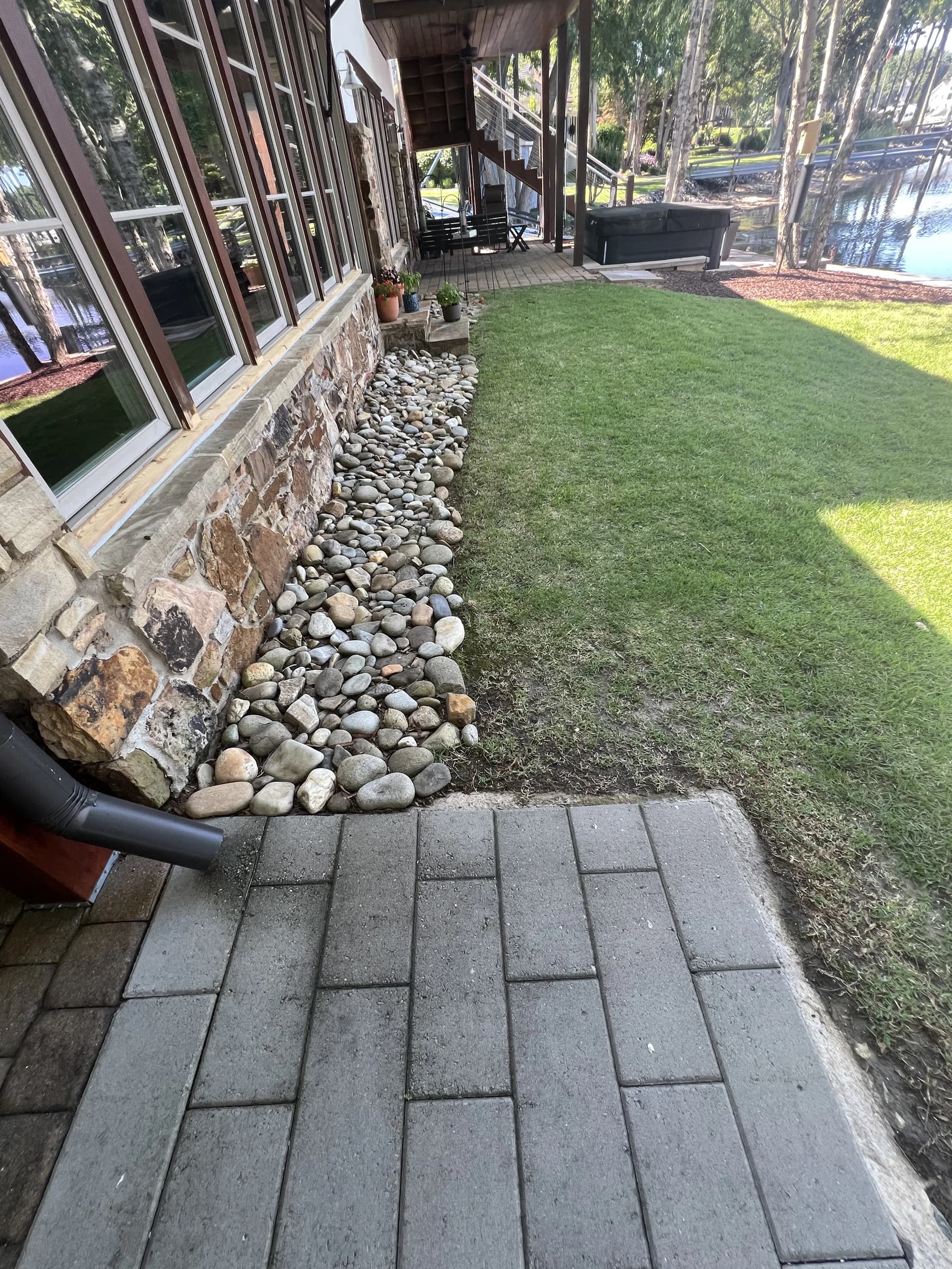 A river-rock drainage border along a stone foundation wall beside a paver walkway