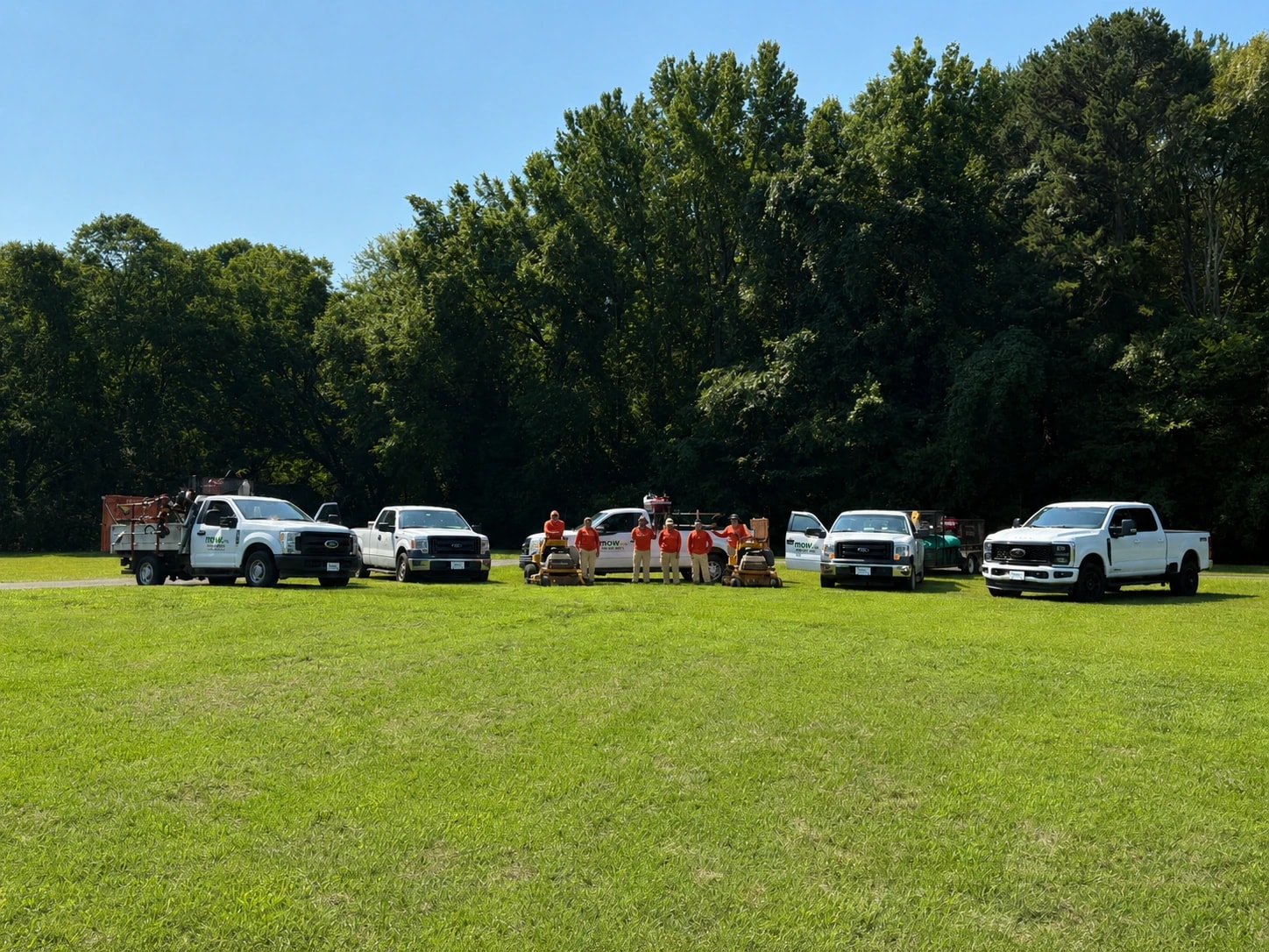 The Mow, Inc. crew standing with the company's trucks and stand-on mowers lined up on a mown lawn